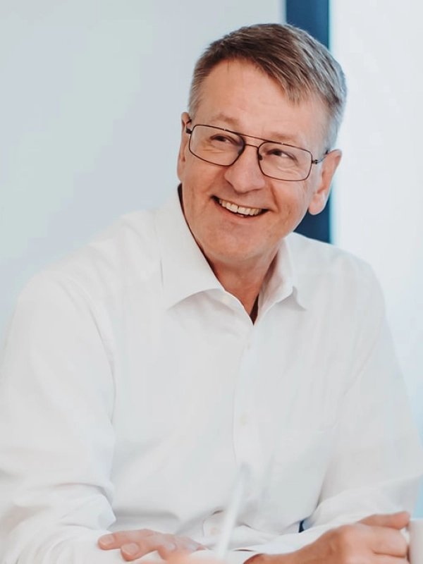 Mann mittleren Alters mit Brille lacht freundlich zur Seite.